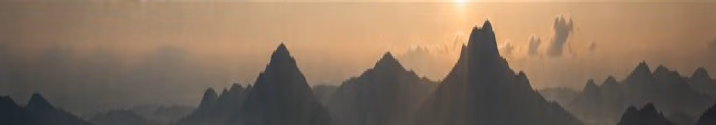 Layered mountains at dusk beneath an amber sky.