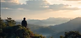 A lone figure overlooking layers of green mountain ridges.